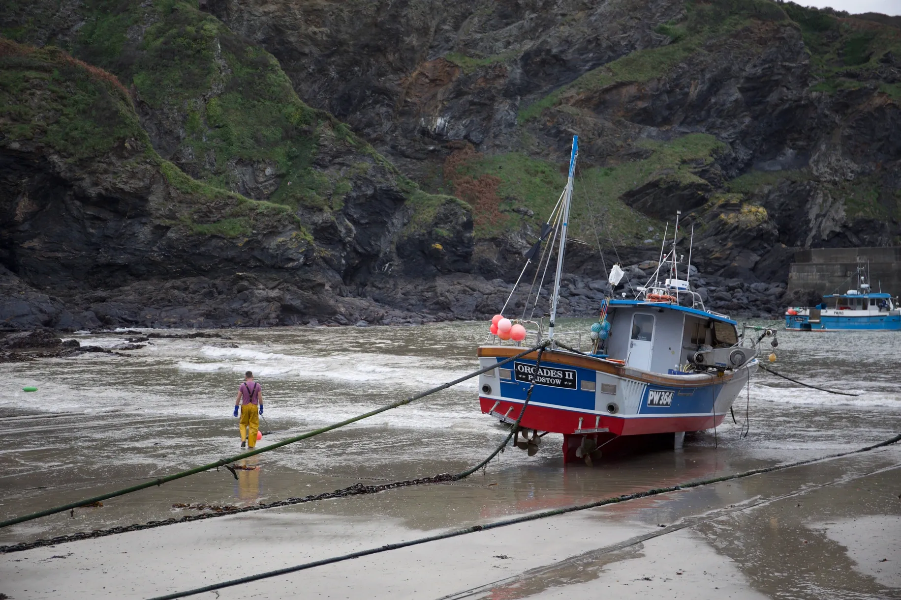 A fishing boat beached on a sandy shore at low tide with a person walking nearby.