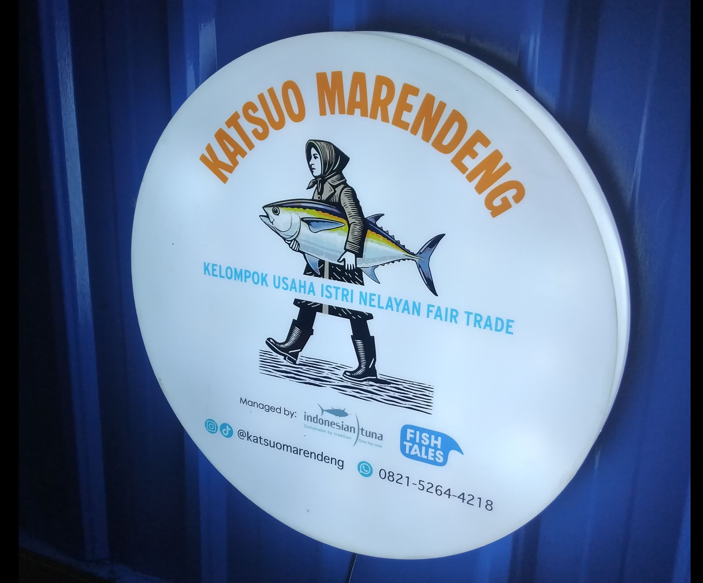 Illuminated round sign for "KATSUO MARENDENG" with a person carrying a large tuna.