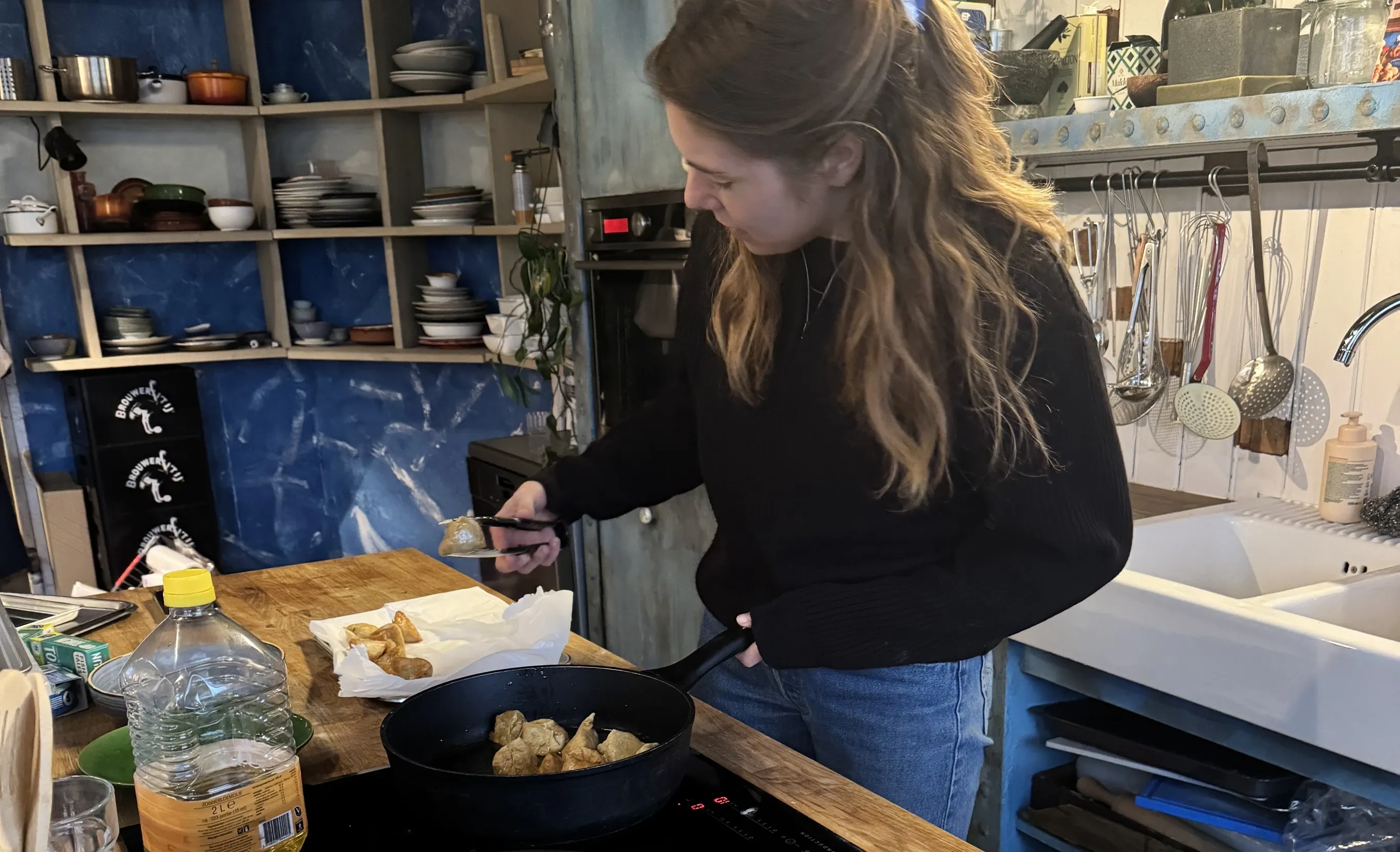 Woman cooking dumplings in a pan with tongs, plate of raw dumplings nearby.