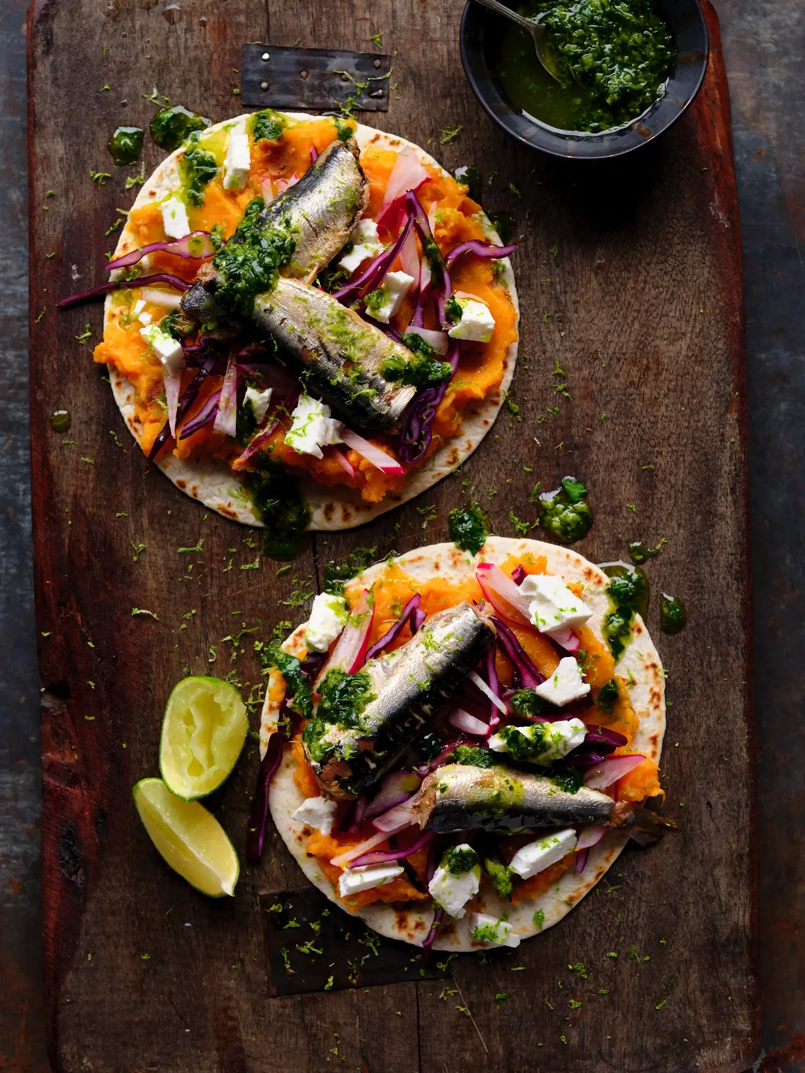 Sardine tacos with sweet potato, red onion, and cilantro on a dark wooden board.